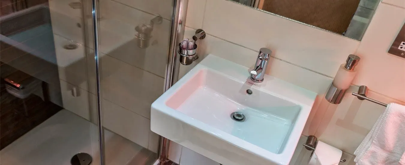 A shower room at Space Apart Hotel with a square white basin, cream tiles, chrome fittings and a walk-in shower behind a glass door