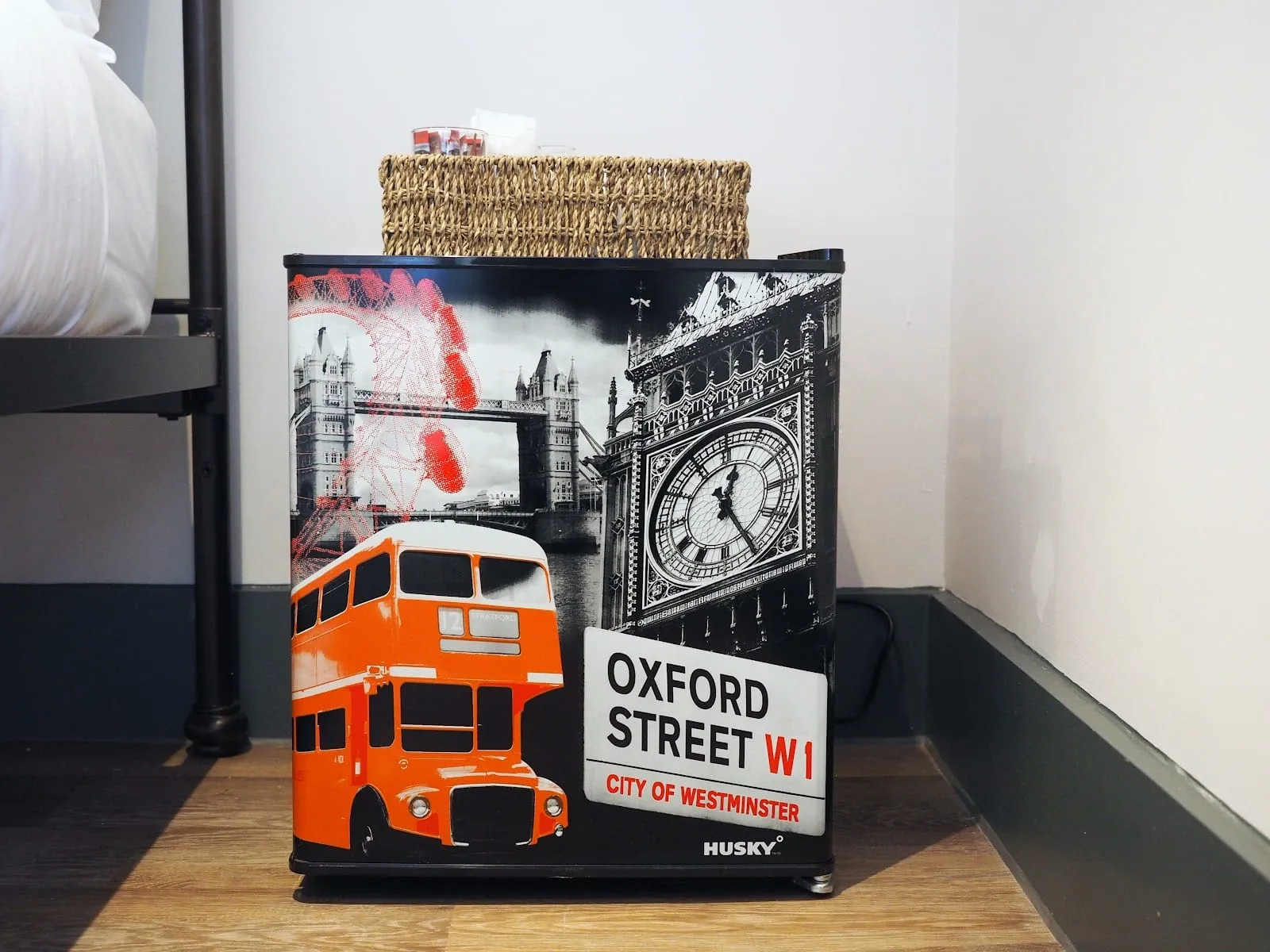 A bedside table at St Christopher's Liverpool Street, with a London-landmarks print on the mini-fridge beside the bed