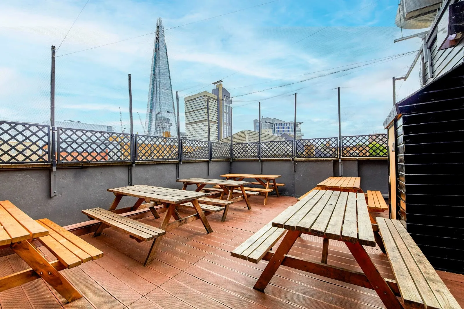 The roof terrace at St Christopher's Village, with wooden picnic tables on decking and the Shard rising behind the railings
