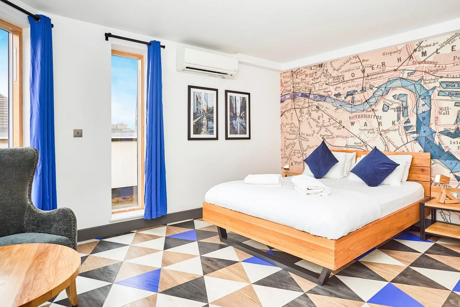 A private double room at St Christopher's Village with a wooden bed against a mural of an old map of the Thames through Southwark and Rotherhithe, a triangle-patterned floor and blue curtains