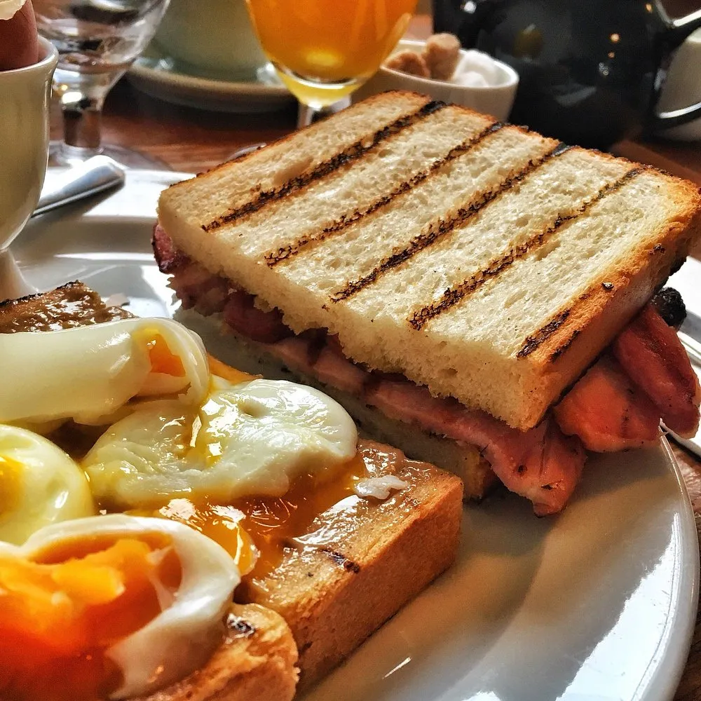 A bacon sandwich in griddled white bread, served with soft-boiled eggs and toast
