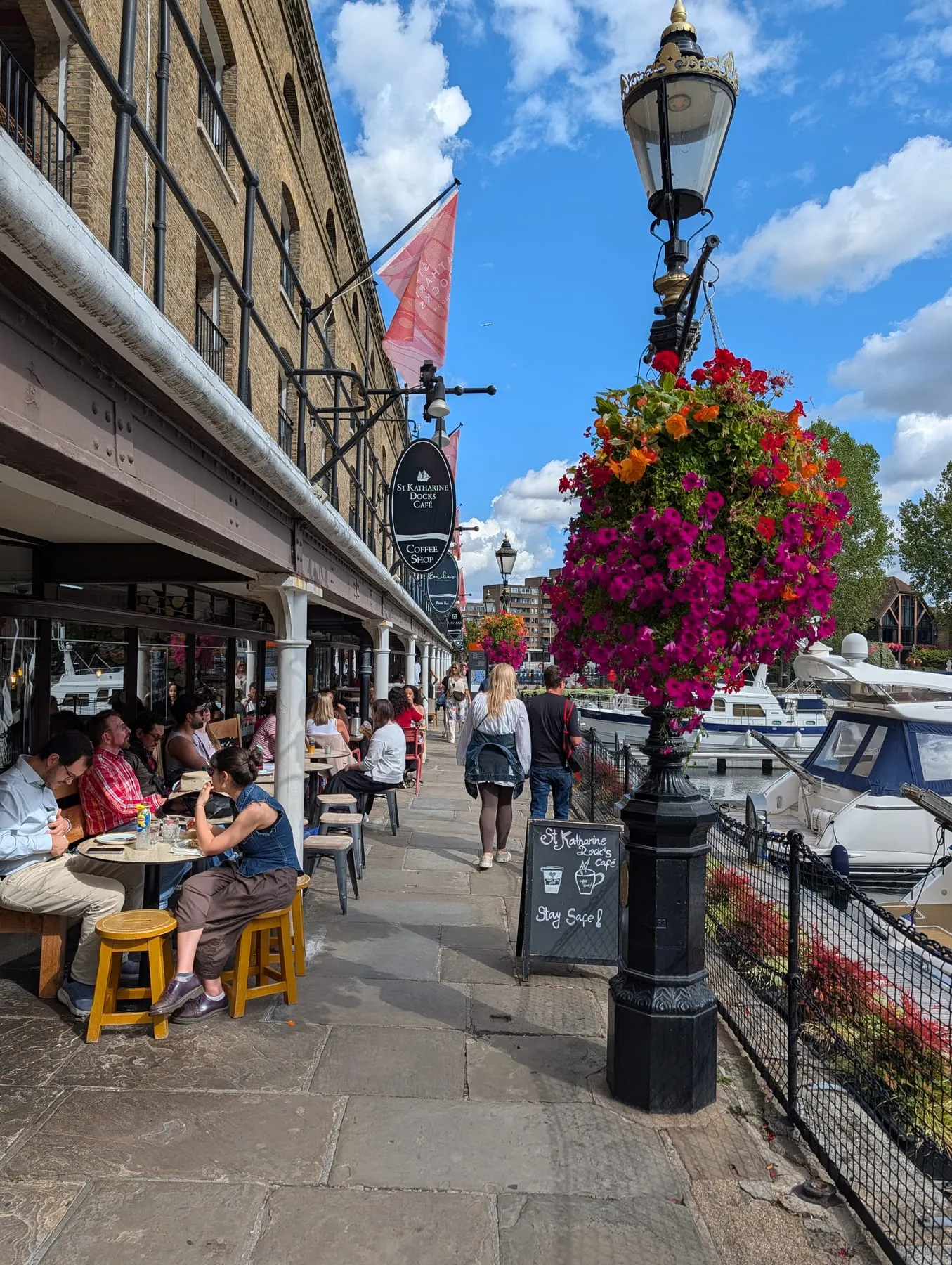 Boats moored at St Katharine Docks with restaurant tables along the quayside opposite