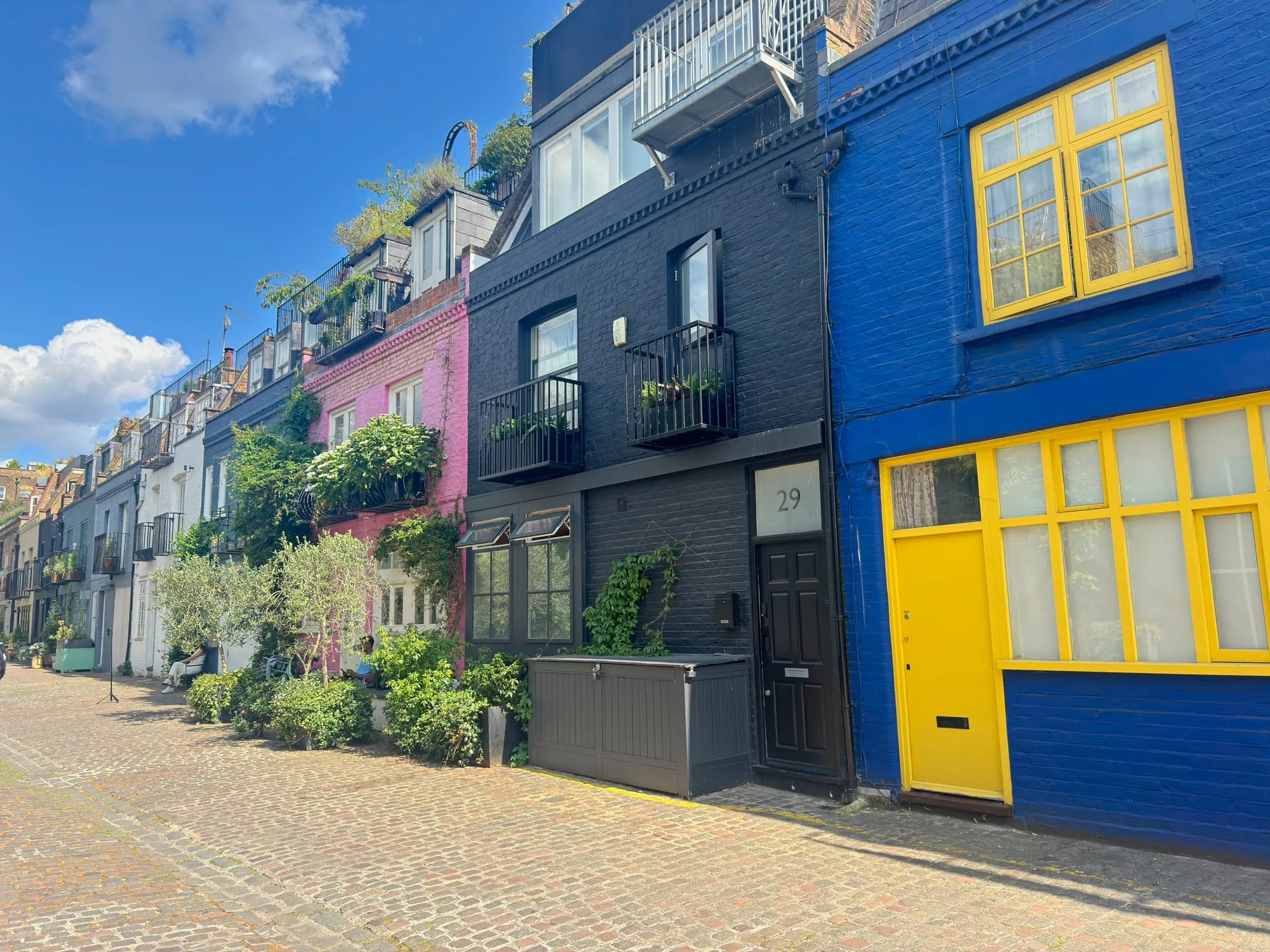 A cobbled mews of houses painted vivid blue, pink and cream with yellow window frames