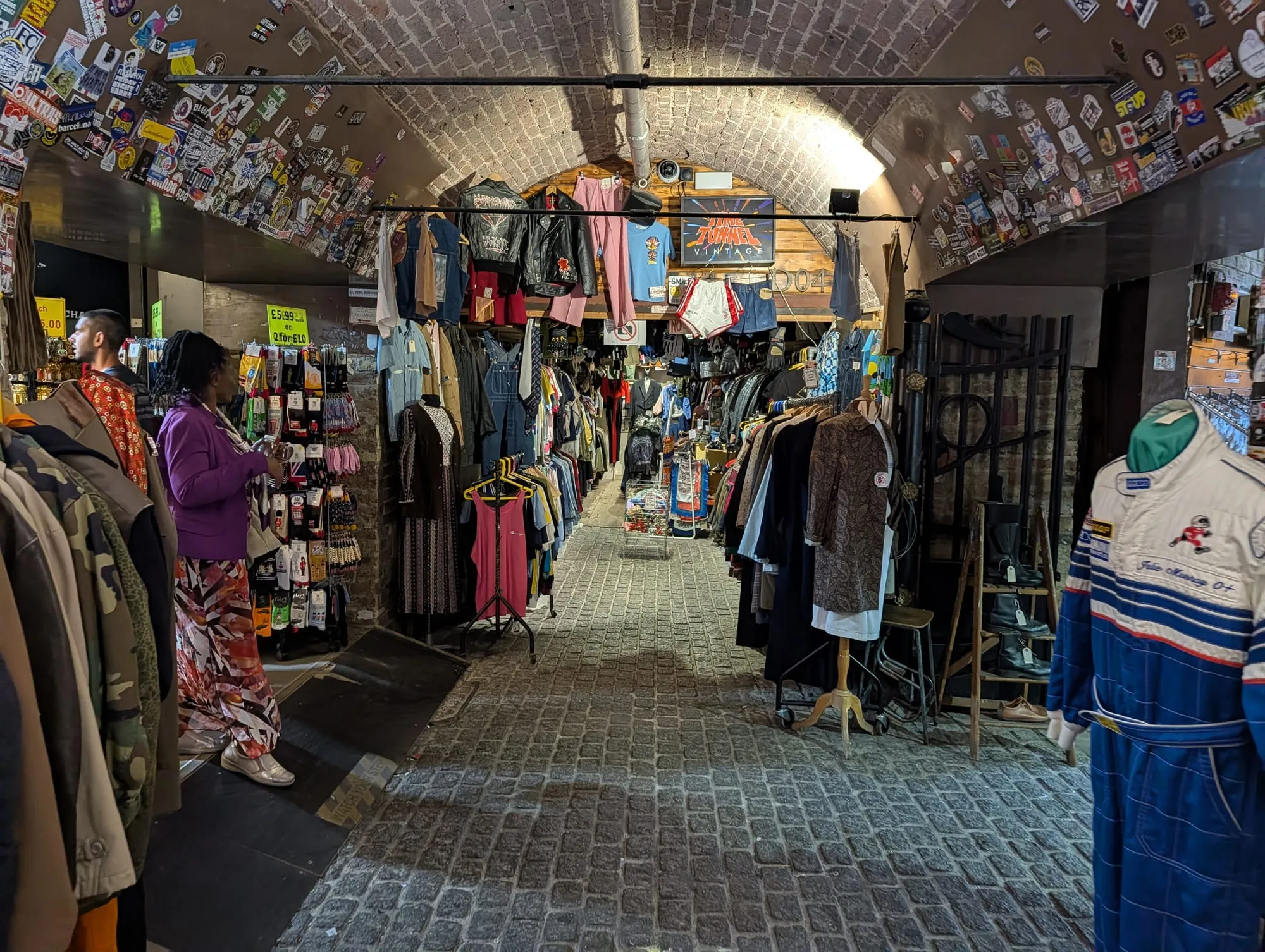 Rails of vintage coats and dresses under a brick railway arch in Camden Stables Market