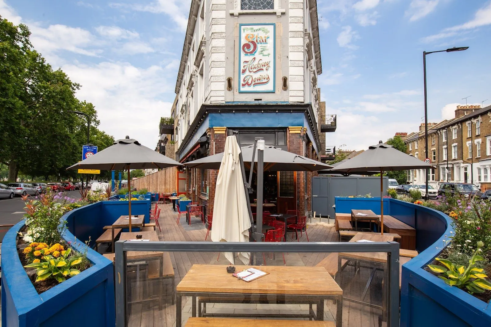 The Star by Hackney Downs, a corner pub with a painted Star Hackney Downs sign, a blue fascia and a planted terrace of tables under parasols