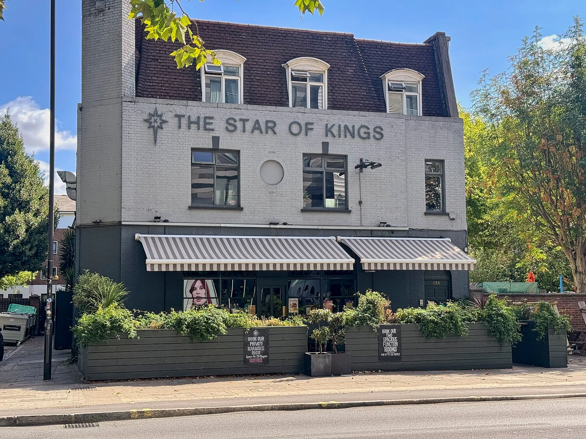 The Star of Kings on York Way, a white-painted pub with grey striped awnings over a planted terrace and a sign advertising its private karaoke room