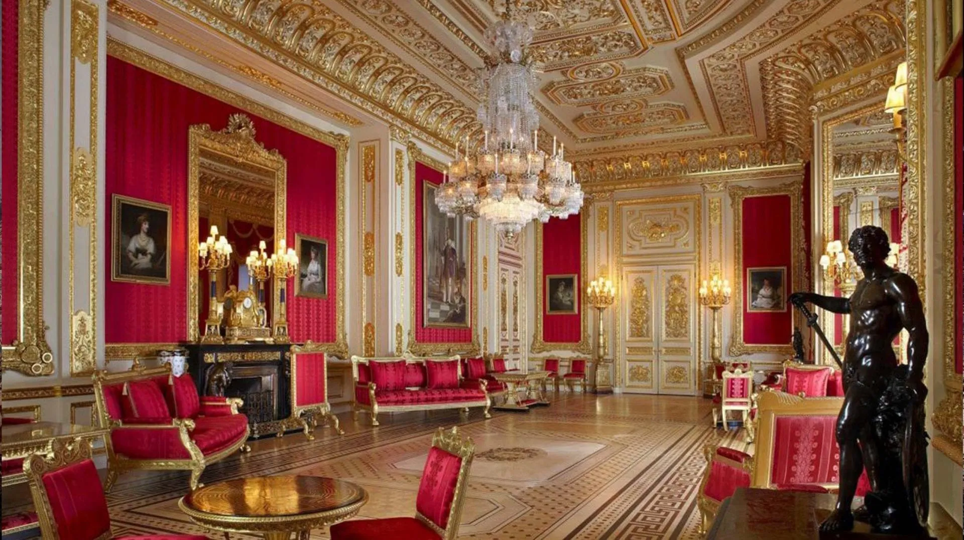A State Apartment at Windsor Castle: crimson walls, gilded ceiling, chandeliers and portraits above a marble fireplace