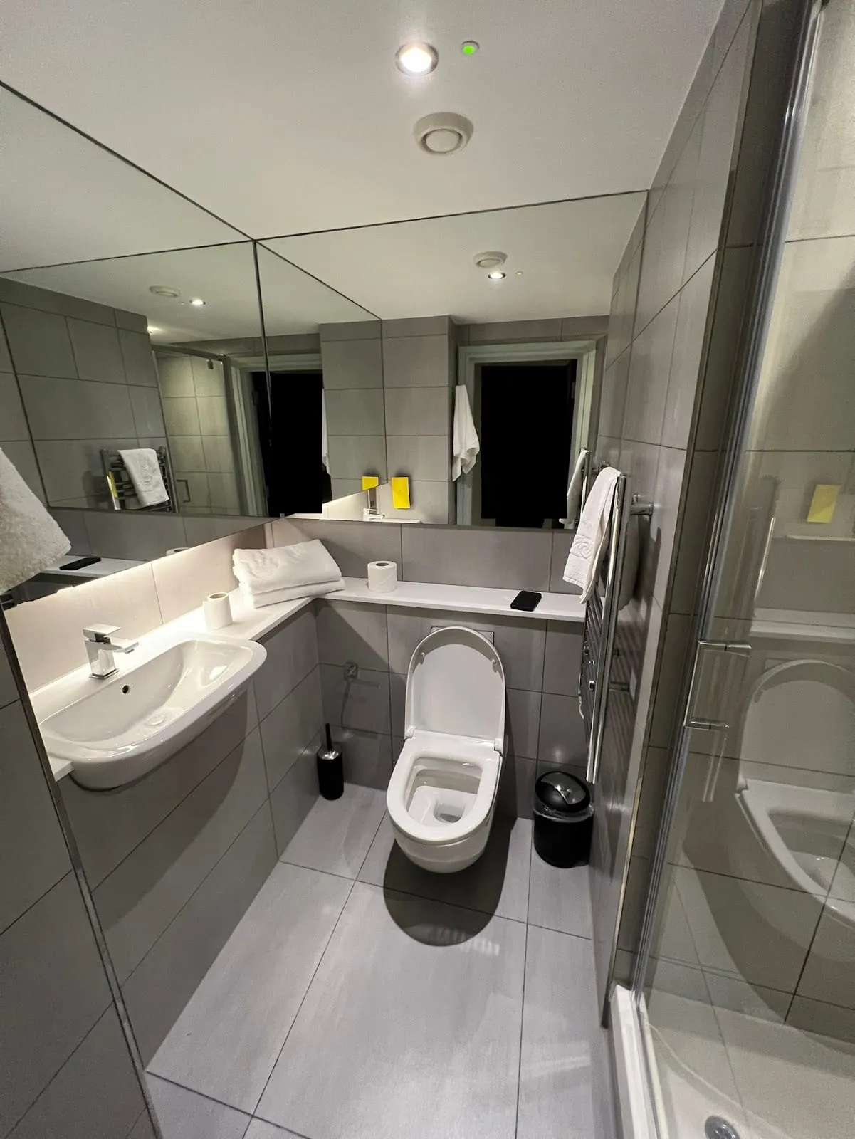The bathroom at Staycity Deptford Bridge, with grey tile, a mirrored wall and a glass-enclosed shower