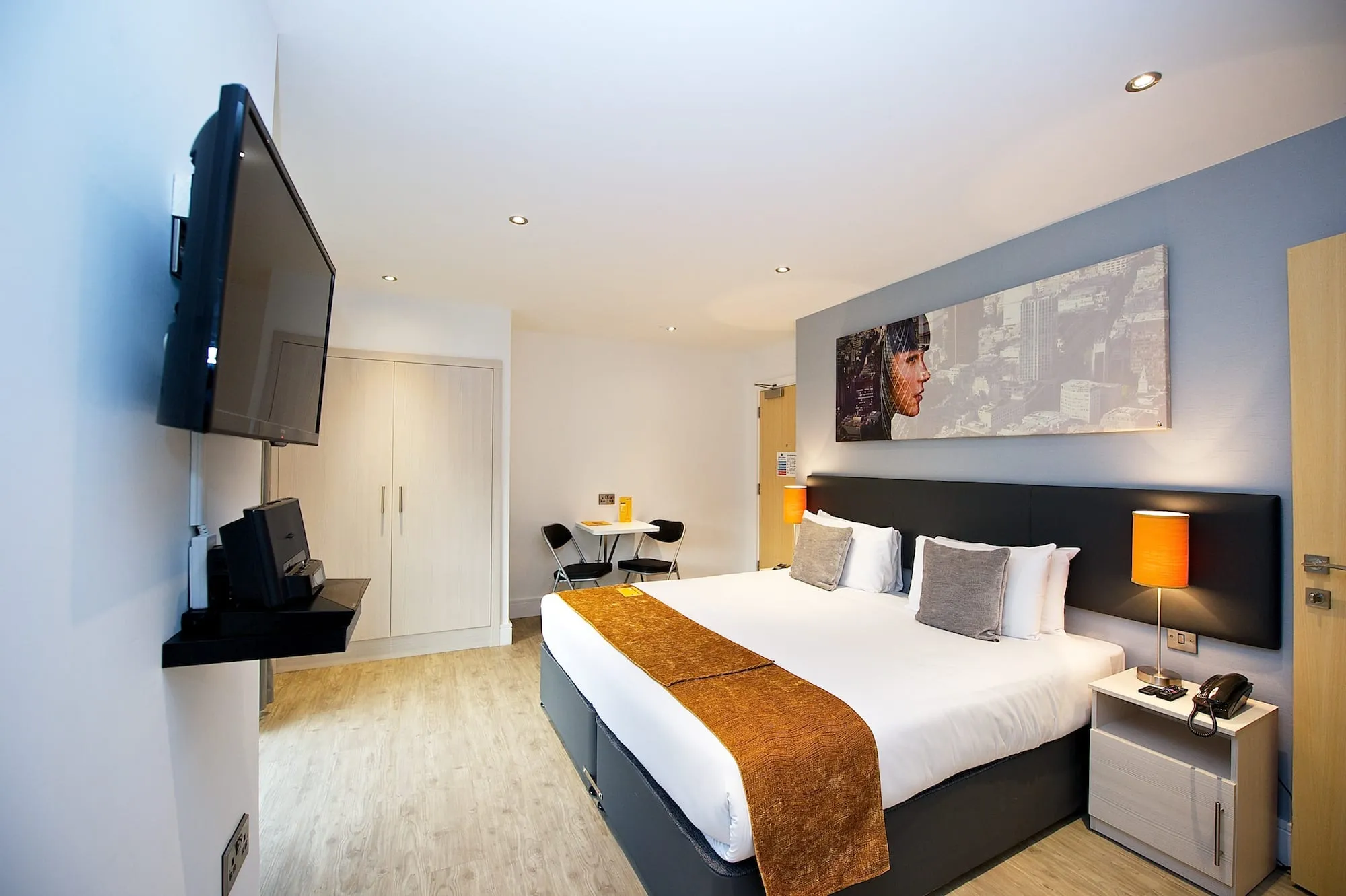 A bedroom at Staycity Deptford Bridge, with a wall-mounted television, a built-in wardrobe and a two-seat table by the window