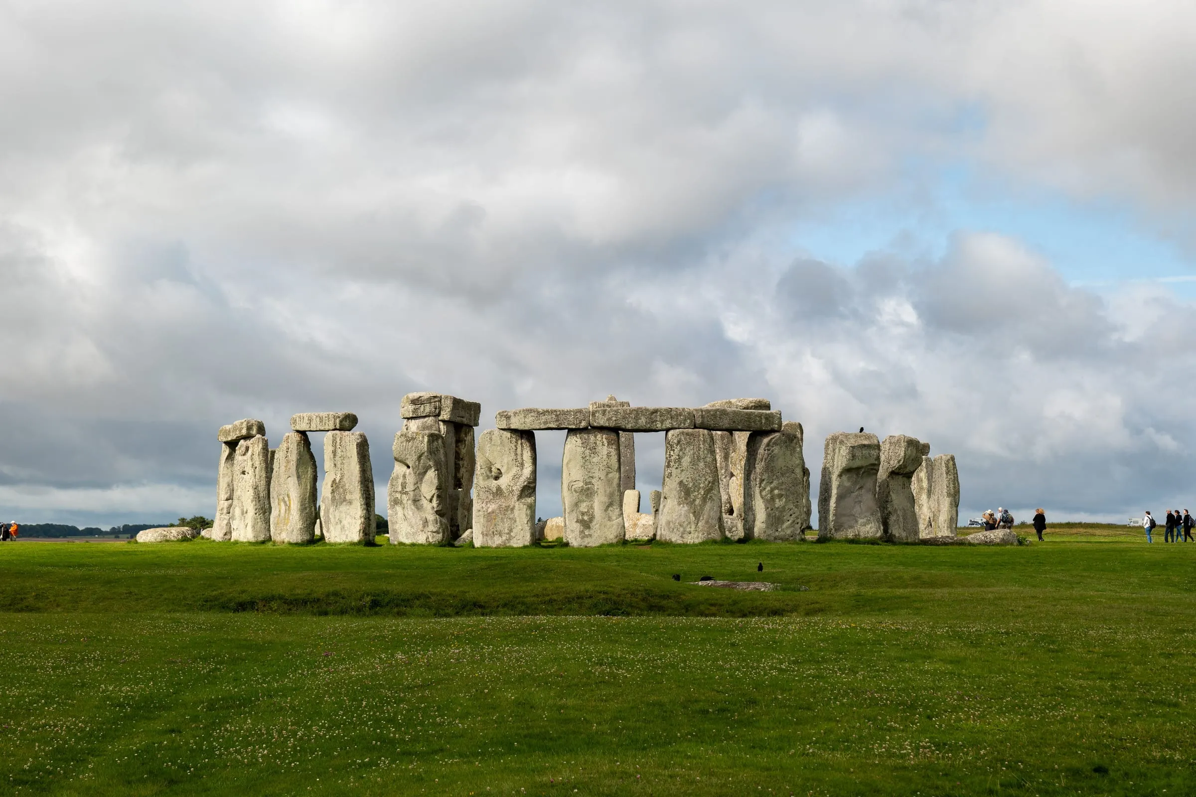 The full Stonehenge circle seen across open grass, the sarsen trilithons and fallen stones under a wide sky