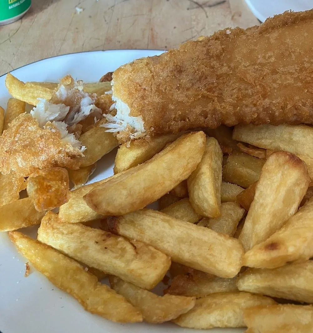 A close-up of a battered fillet broken open at Stones Fish and Chips, showing white flakes inside a crisp golden crust, beside thick hand-cut chips