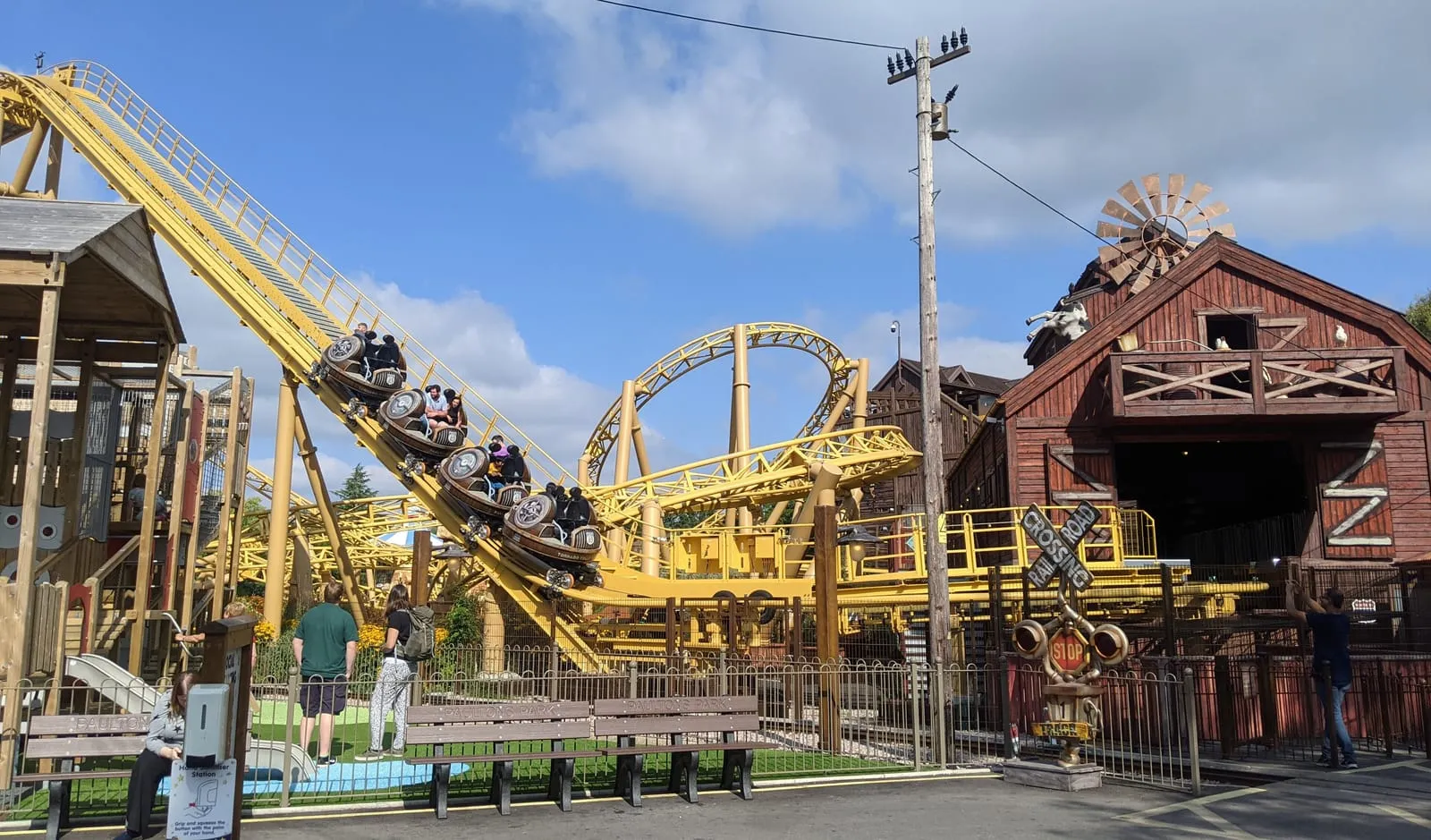 The Storm Chaser spinning coaster at Paultons Park, its cars climbing the lift hill beside a yellow steel loop and a wooden barn