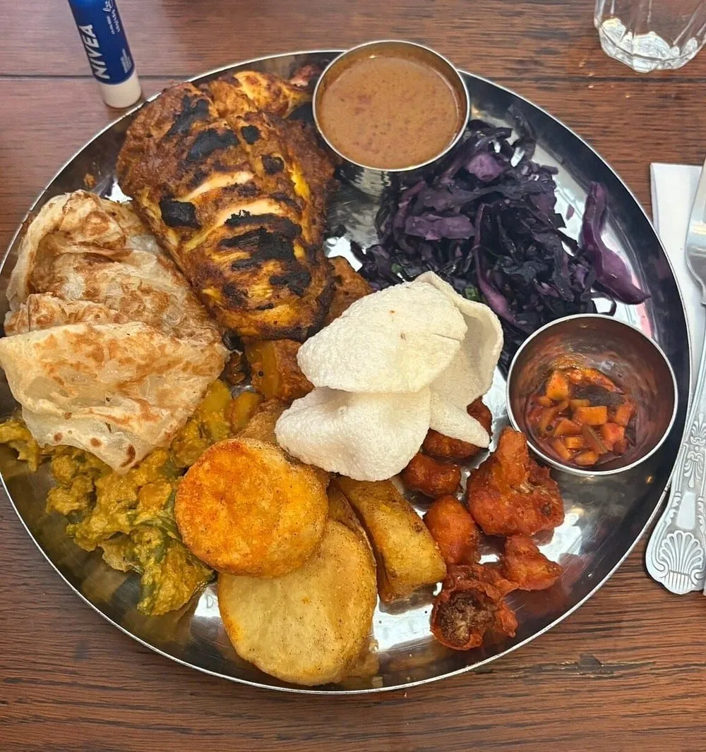 The Tamil Crown Sunday roast on a steel thali: tandoori chicken, roast potatoes, parathas, poppadoms, red cabbage and curry sauces