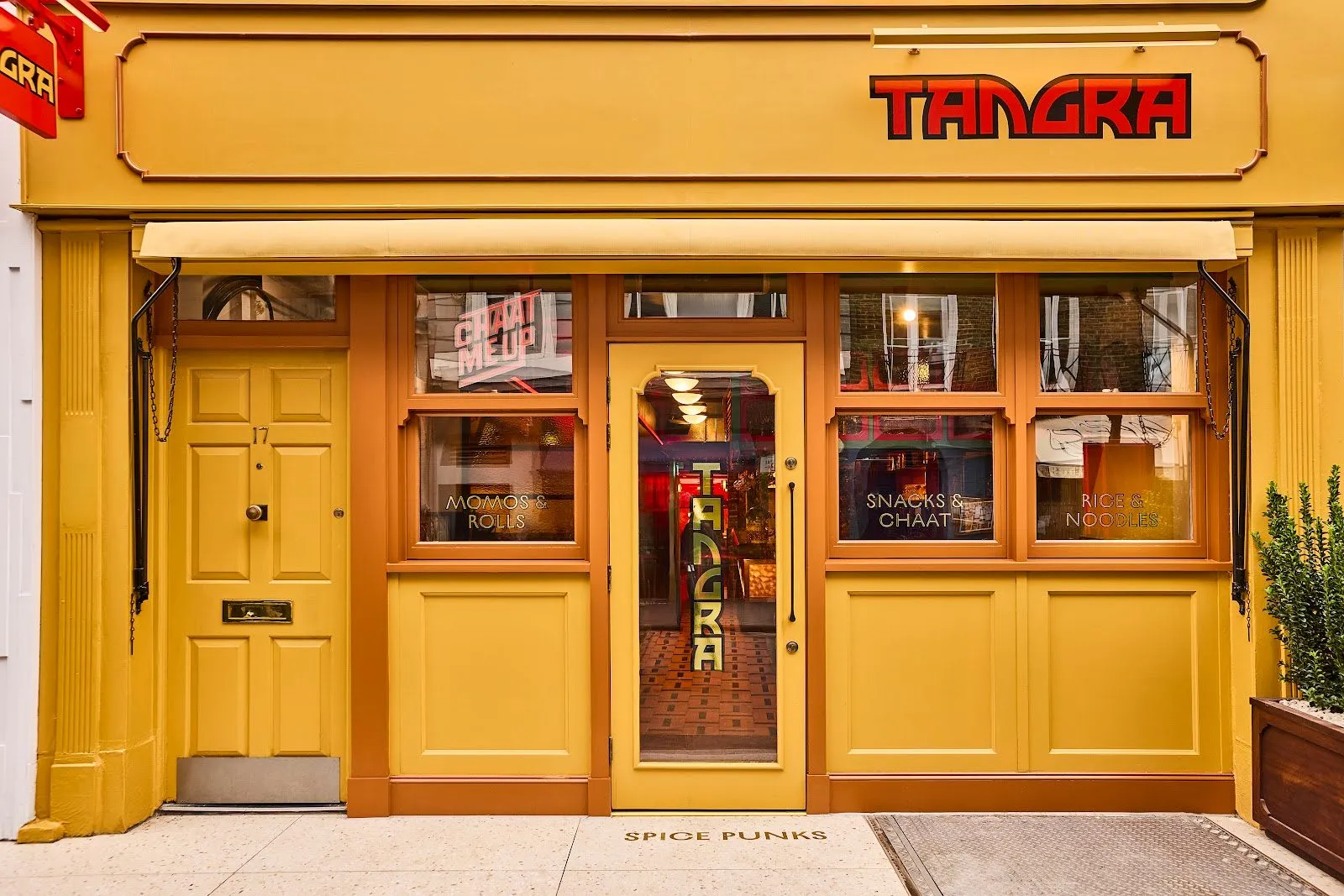 The mustard-yellow shopfront of Tangra at 17 Frith Street, with the name in red lettering and window panels reading momos and rolls, snacks and chaat, rice and noodles