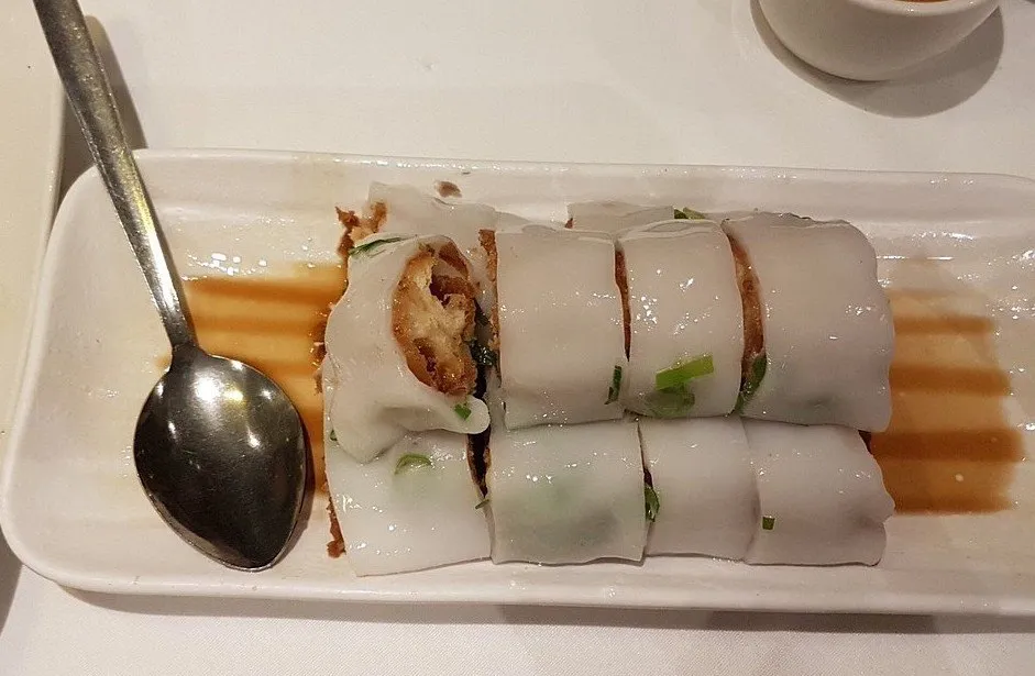 Cheung fun rice noodle rolls filled with fried dough sticks, sliced and sitting in sweet soy on a long white plate