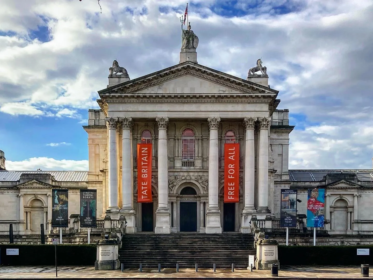 The Portland stone facade of Tate Britain with orange Tate Britain and Free for All banners hanging between the columns