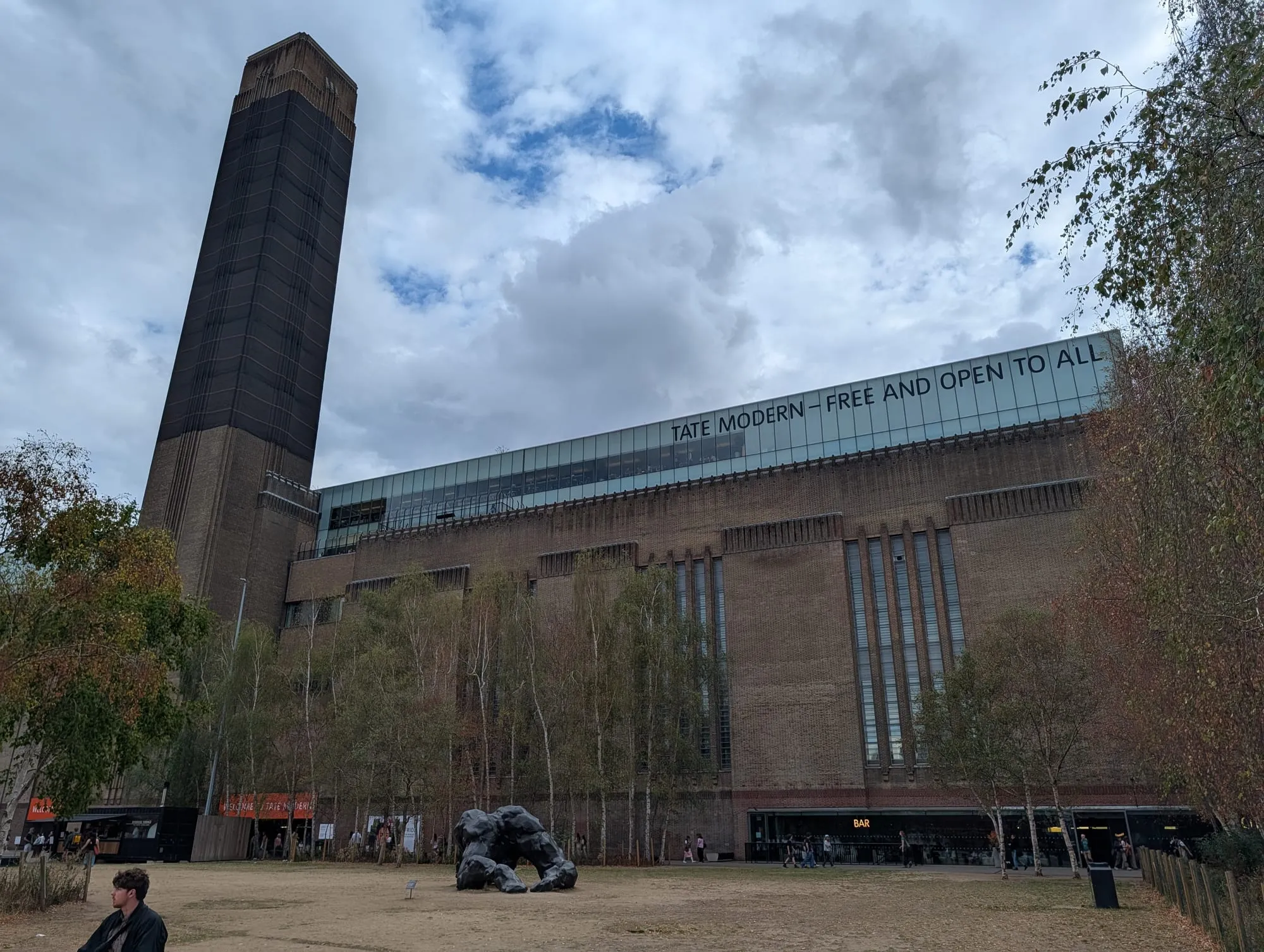 The brick chimney and long riverside frontage of Tate Modern, with a banner reading free and open to all