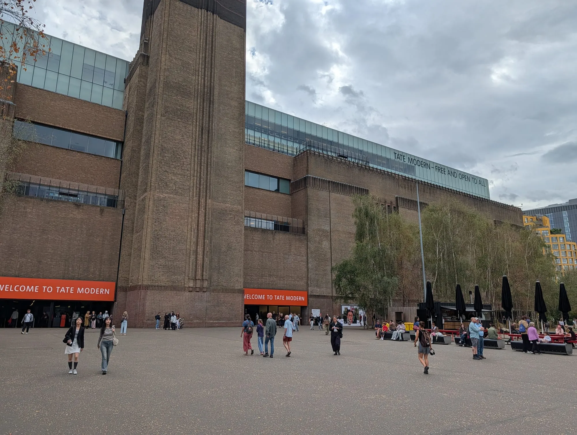 The brick flank and chimney of Tate Modern from the riverside, with a sign along the roofline reading Tate Modern - free and open to all