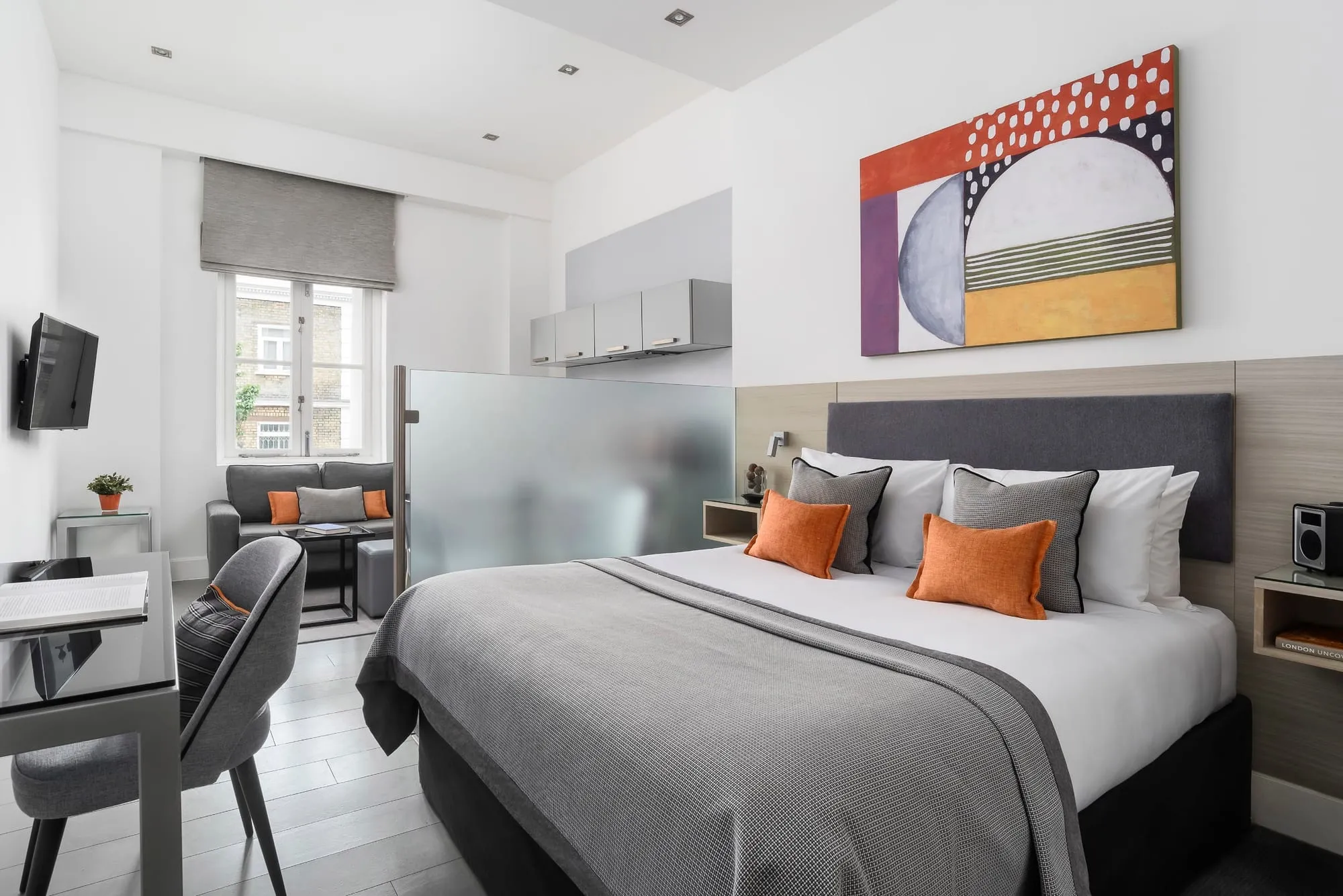 A studio at Templeton Place, with a frosted-glass partition separating the bed from a small kitchenette, plus a sofa and armchair by the window