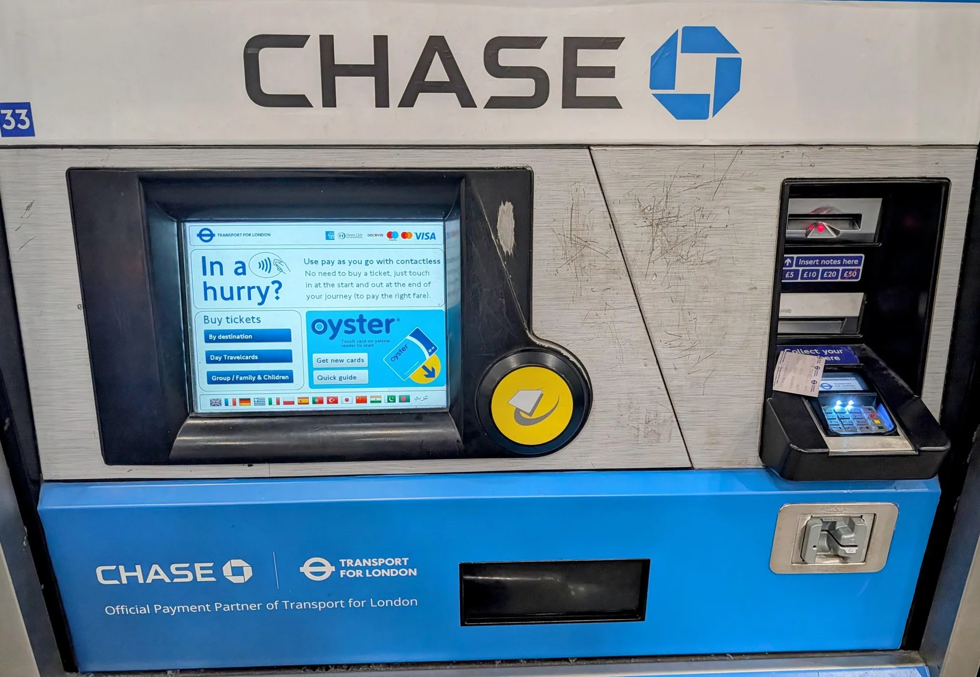 A Chase-branded Transport for London ticket machine showing the Oyster top-up screen and a contactless prompt reading In a hurry?