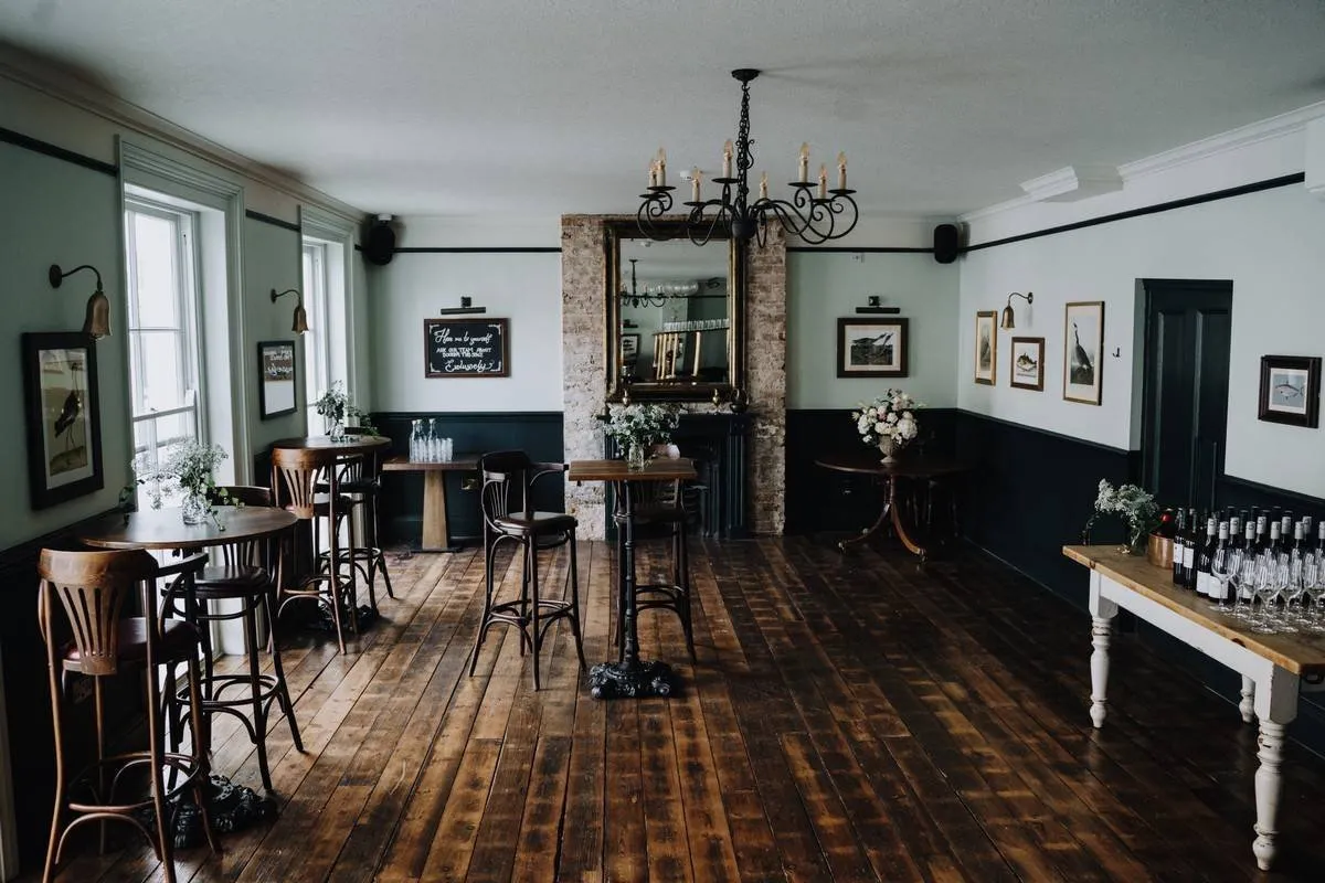 A room at The Admiral Hardy with high tables, bare floorboards, a gilt mirror and framed bird prints