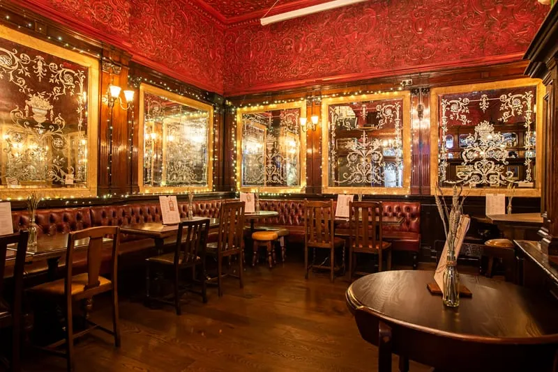 A row of large gilt-framed mirrors and etched glass screens dividing red-walled booths inside The Argyll Arms