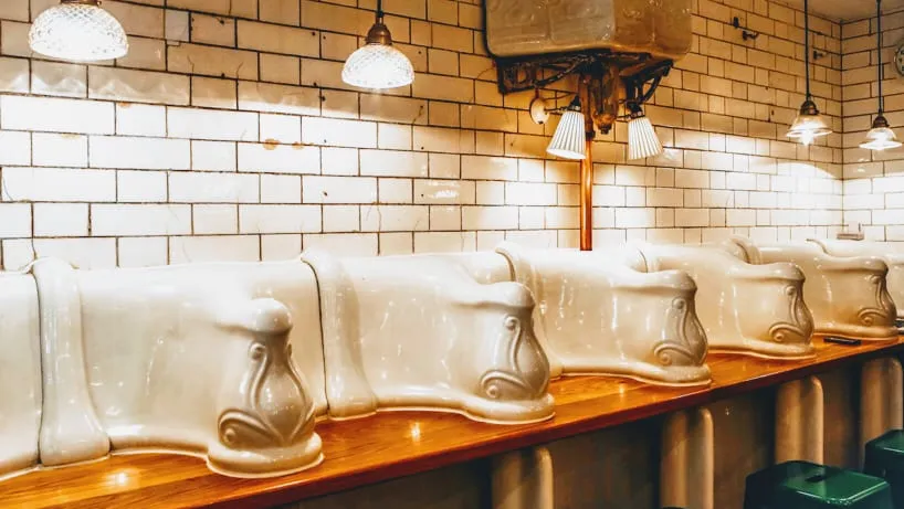 A row of converted Victorian porcelain urinals, now the counter at The Attendant, against white tiled walls