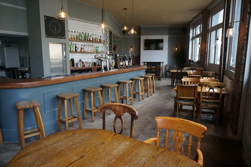 The Baring's bar: a blue panelled counter, wooden stools and tables by tall windows