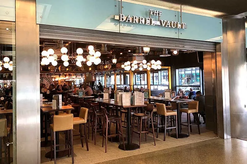 The entrance to The Barrel Vault inside St Pancras International, with rows of barrel-shaped light fixtures hanging above the bar