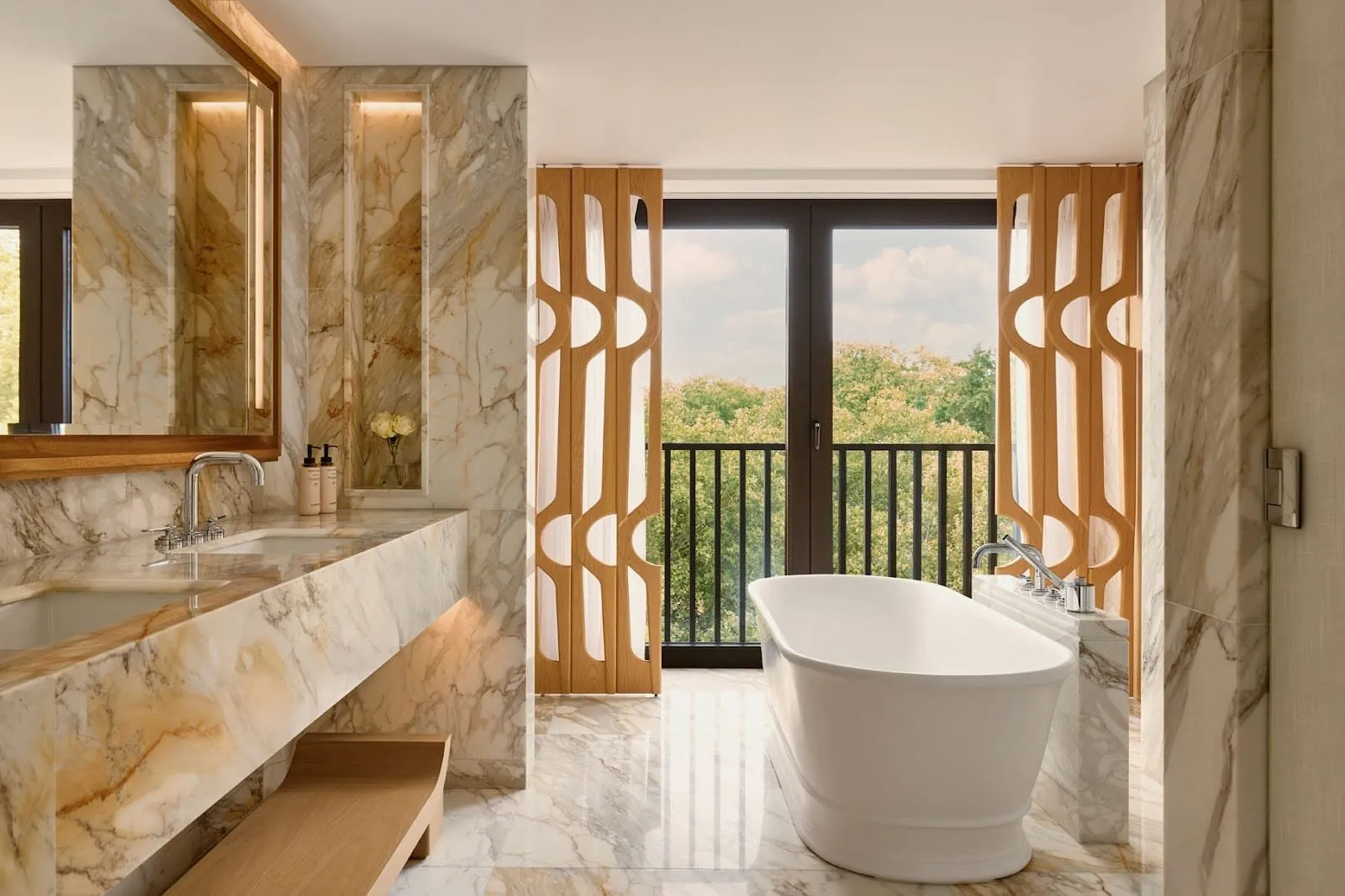 A marble bathroom in the Knightsbridge Pavilion Penthouse at The Berkeley, with a freestanding bath, twin basins, carved oak screens and French windows onto a balcony above the trees