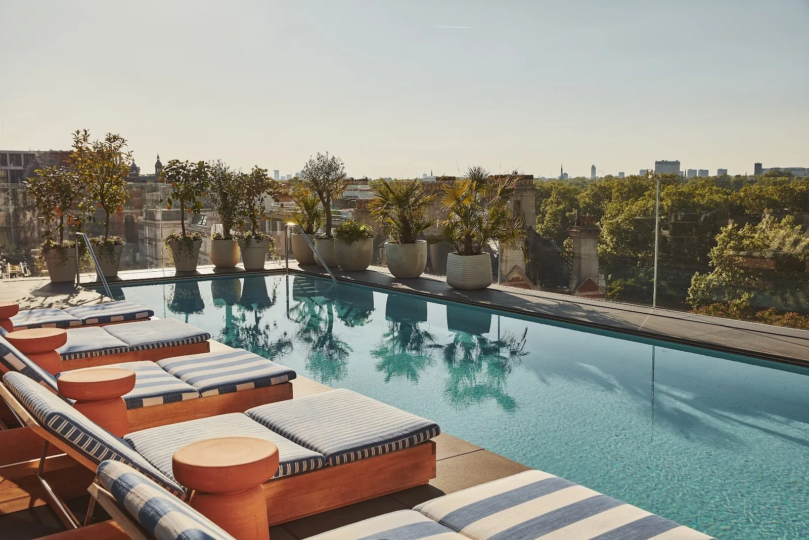 The rooftop swimming pool at The Berkeley with striped sun loungers and views across the treetops of Hyde Park