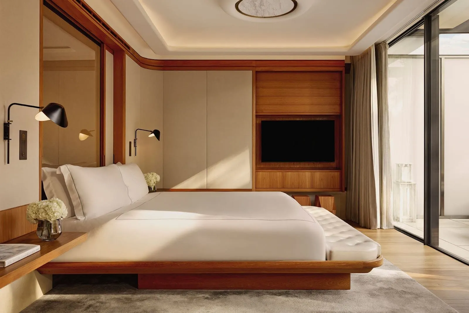 The bedroom of the Grand Terrace Suite at The Berkeley: a low wooden platform bed with white linen, a leather bench at its foot, wood-panelled walls and floor-to-ceiling sliding doors onto a private terrace
