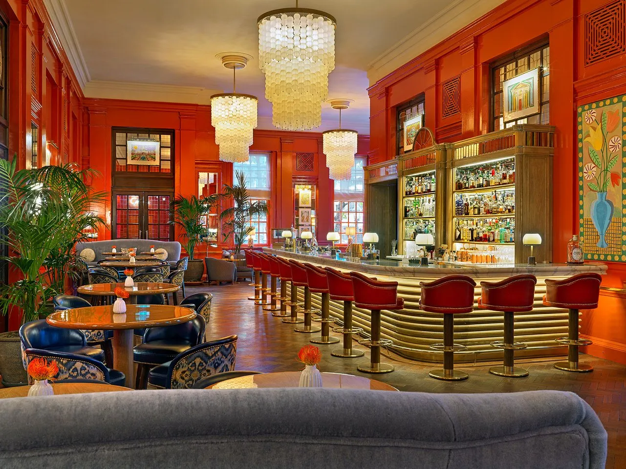 The Coral Room salon bar at The Bloomsbury Hotel with high coral-red walls, brass chandeliers, velvet banquettes and a long bar