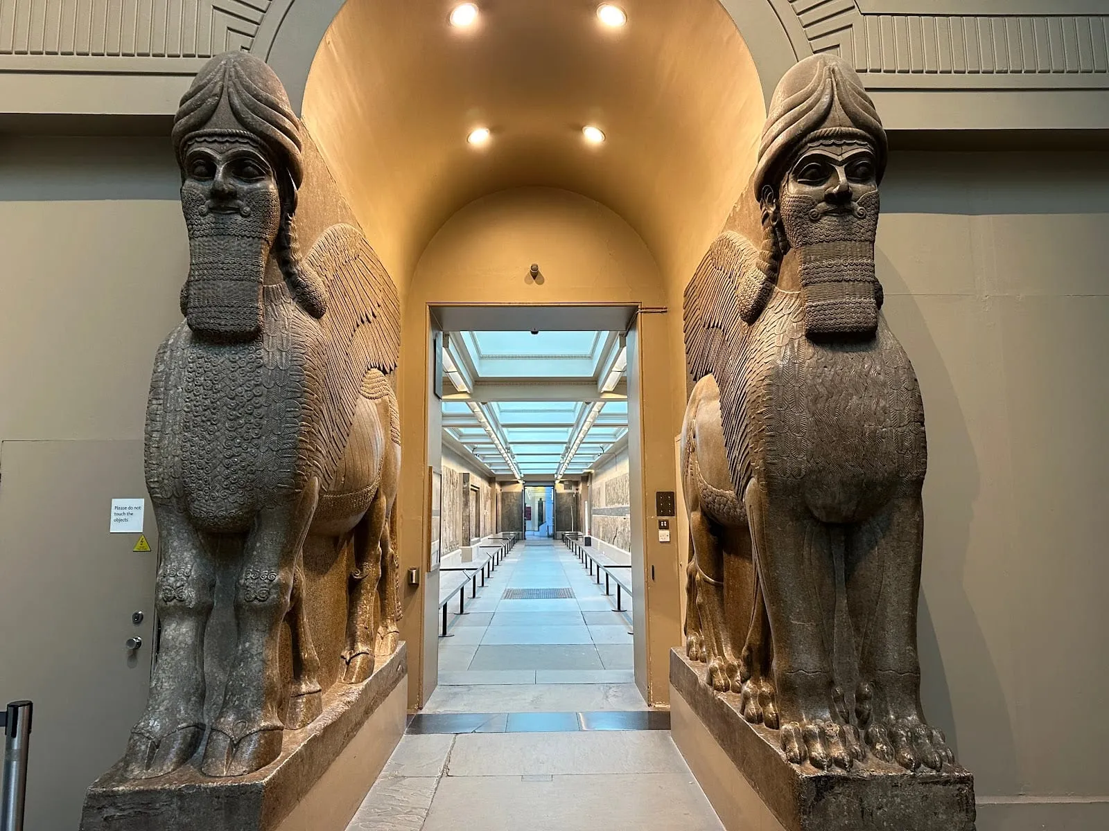Two large stone Assyrian lamassu, winged bulls with human heads, flanking the entrance to a museum gallery
