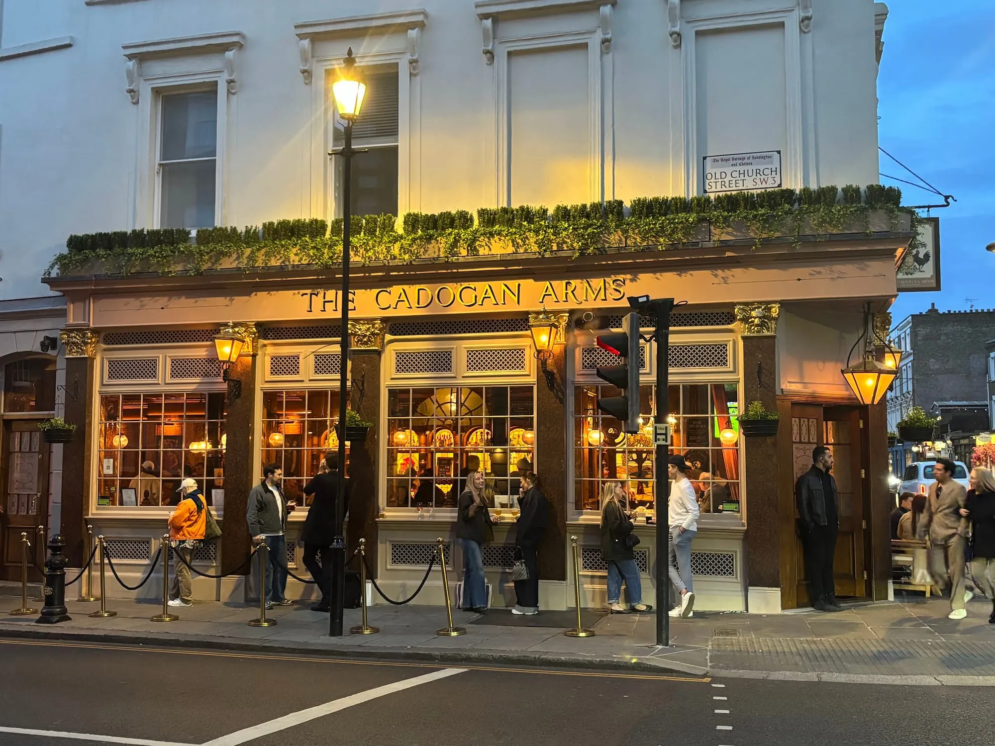 The Cadogan Arms at dusk on the corner of Old Church Street in Chelsea, its windows lit and drinkers outside
