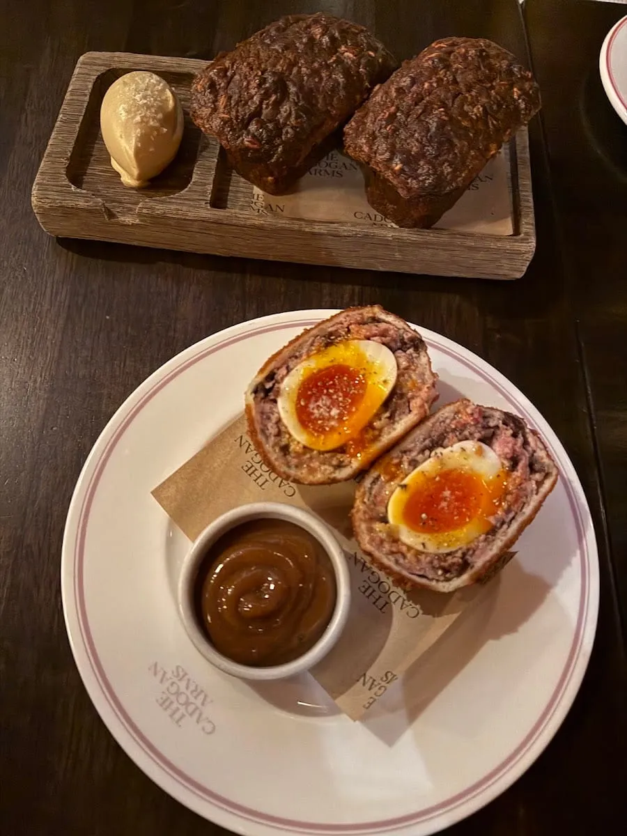 A black pudding Scotch egg cut in half, showing the soft egg yolk inside, on a plate marked The Cadogan Arms