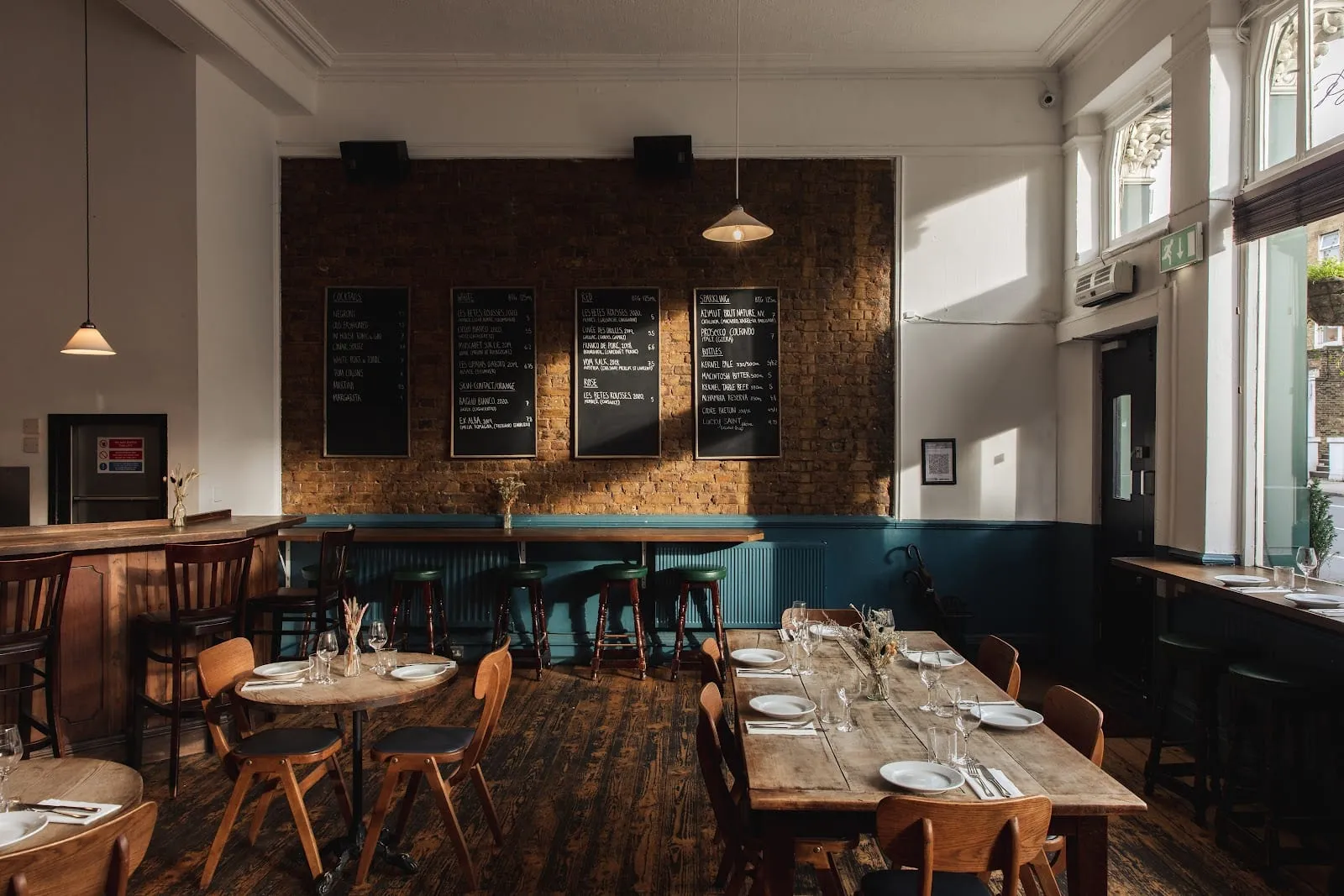 The dining room at The Camberwell Arms, with wooden tables, bentwood chairs and blackboards listing the wine and cocktail list on a brick wall