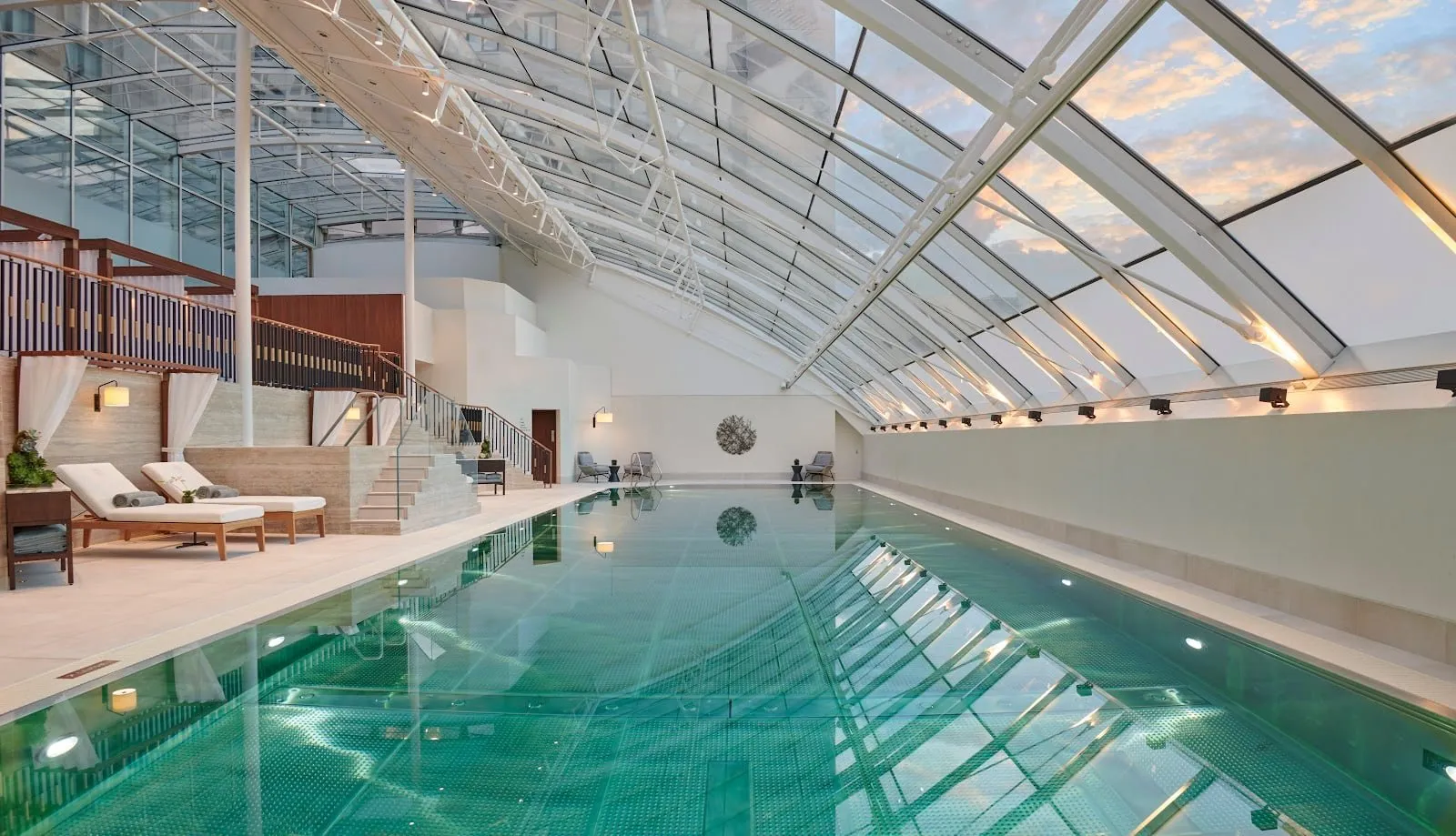 The indoor pool at The Carlton Tower Jumeirah, under a sloping glass roof, with loungers along one side