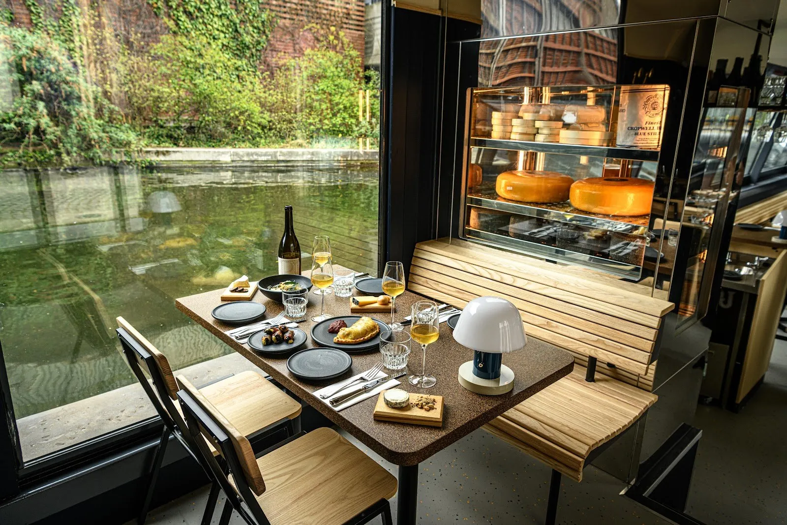 A table set for two beside the window of The Cheese Barge, with a cheese counter behind