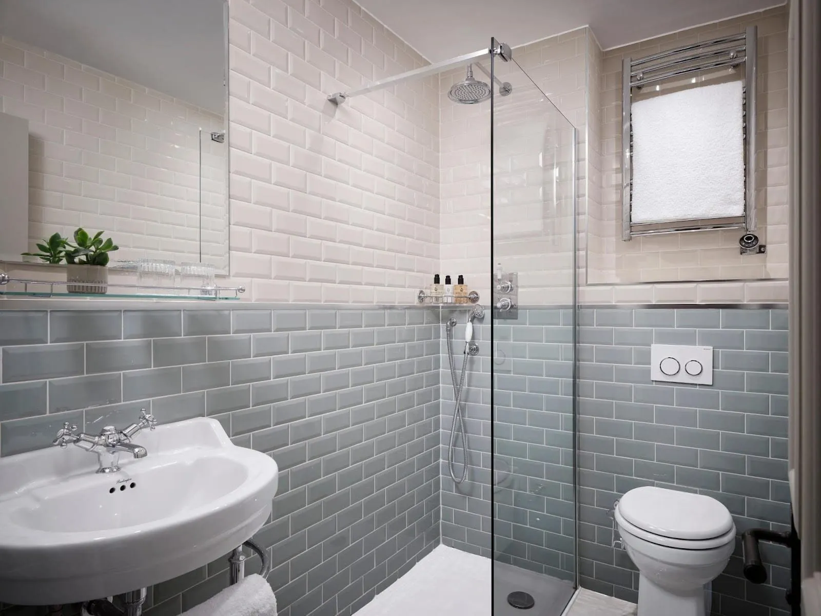 The Chelsea Double's bathroom at The Chelsea Townhouse, in cream and grey-green metro tiles, with a walk-in shower behind a glass screen, a rainfall head, a white basin and a heated towel rail