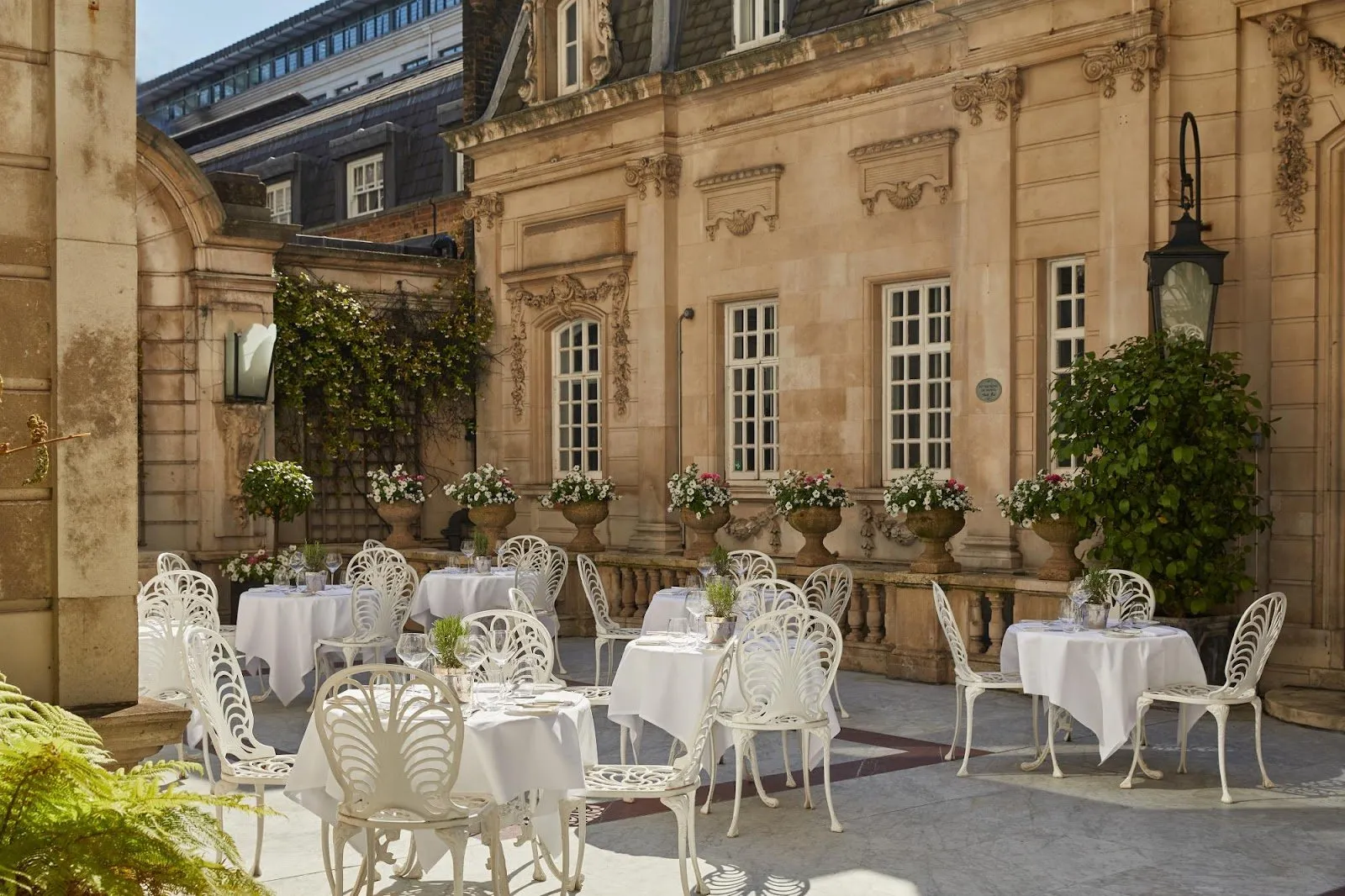 The stone courtyard terrace at The Chesterfield Mayfair, with white ironwork chairs and potted flowers against the townhouse facade