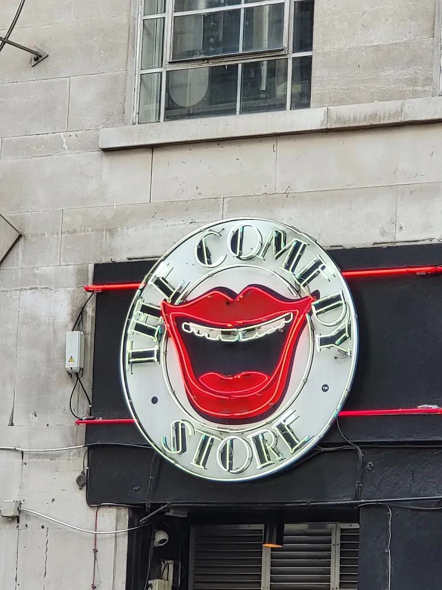 The circular neon sign of The Comedy Store, showing a pair of red lips and the club's name, mounted on a stone building