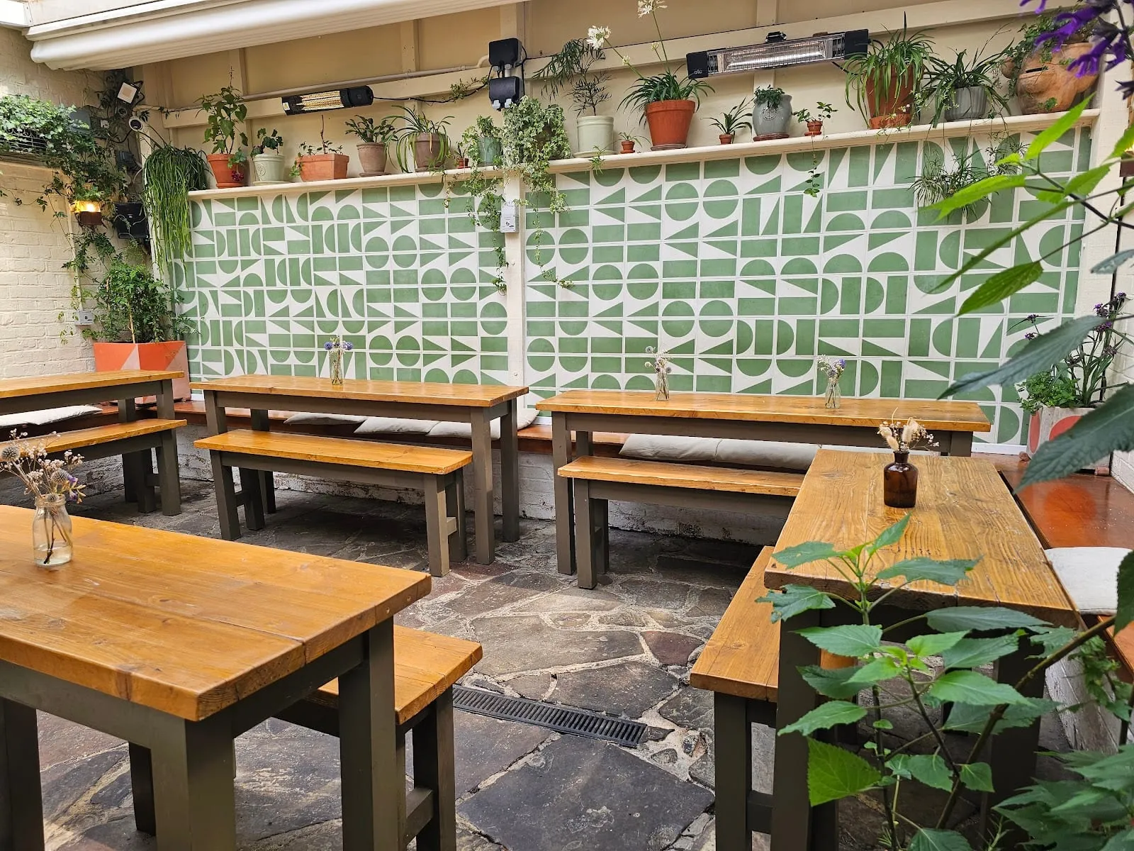 The courtyard at the back of The Compton Arms, with wooden benches, potted plants and patterned tiles