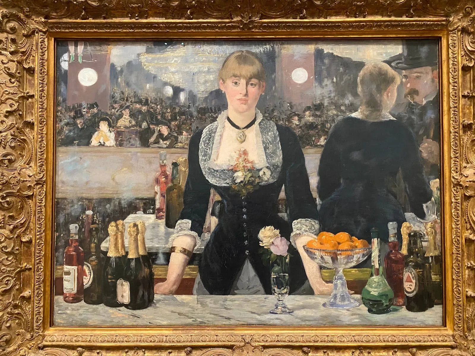Manet's painting A Bar at the Folies-Bergère, showing a barmaid behind a marble counter with bottles and a bowl of oranges, reflected in a mirror behind her