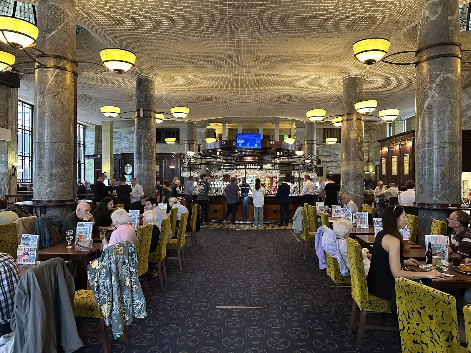 A long marble-columned banking hall with a bar at the far end and diners at tables