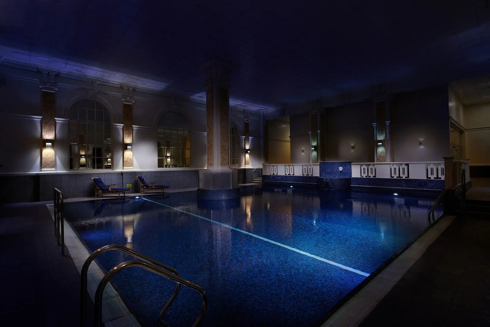 The indoor pool at The Dilly, lit blue, with arched windows on the wall beyond