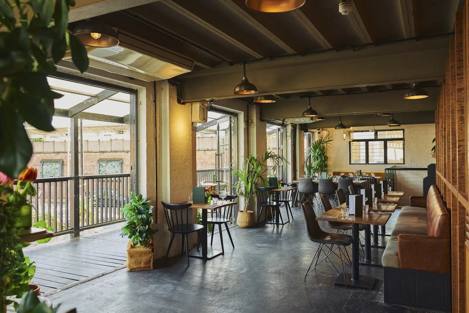 The restaurant at The Exhibit, with wooden tables, leather banquettes, pendant lamps, pot plants and glazed doors onto a balcony