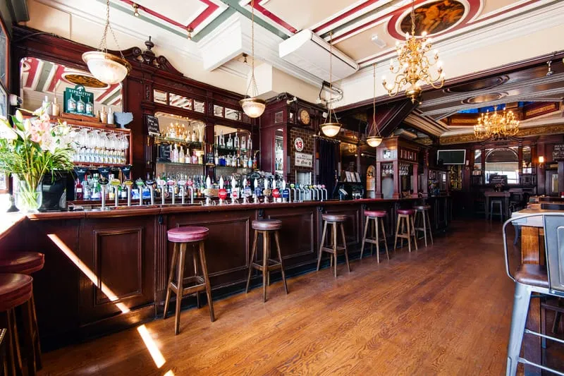 The Flying Horse's bar beneath a decorative fan-striped ceiling in red, green and cream, with wood stools and pendant lights
