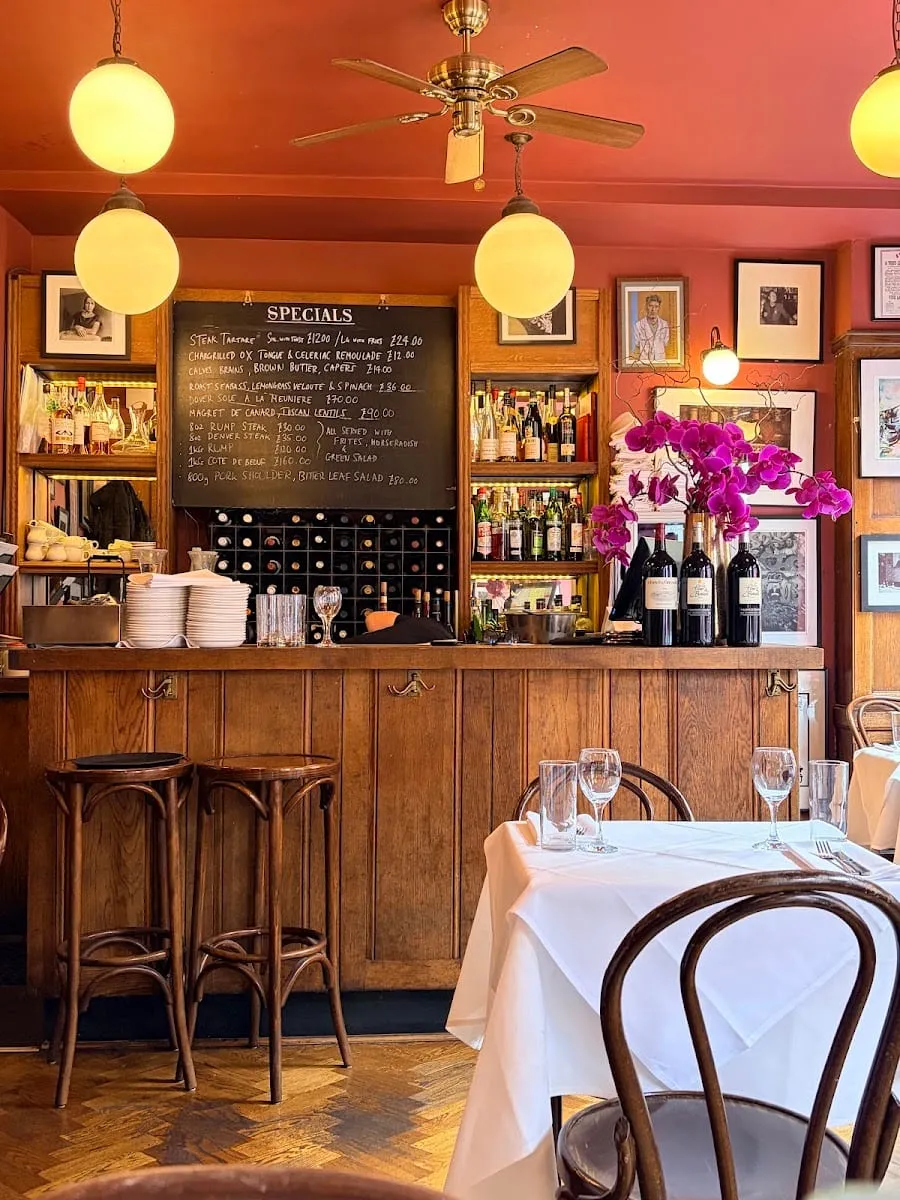 The upstairs dining room at The French House, with a chalkboard of specials, dark wood panelling, wine bottles and an orchid on the bar
