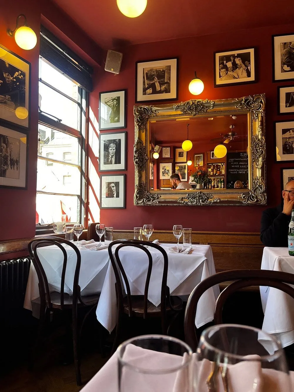 The upstairs dining room at The French House, red walls hung with framed black-and-white photographs around an ornate silver mirror, with bentwood chairs and white-clothed tables